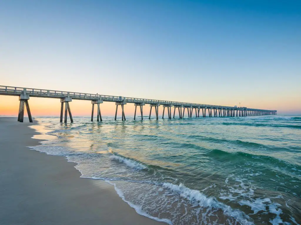 Panama City Beach, Florida, con un muelle que conduce a la distancia al amanecer con la playa y aguas tranquilas en primer plano.