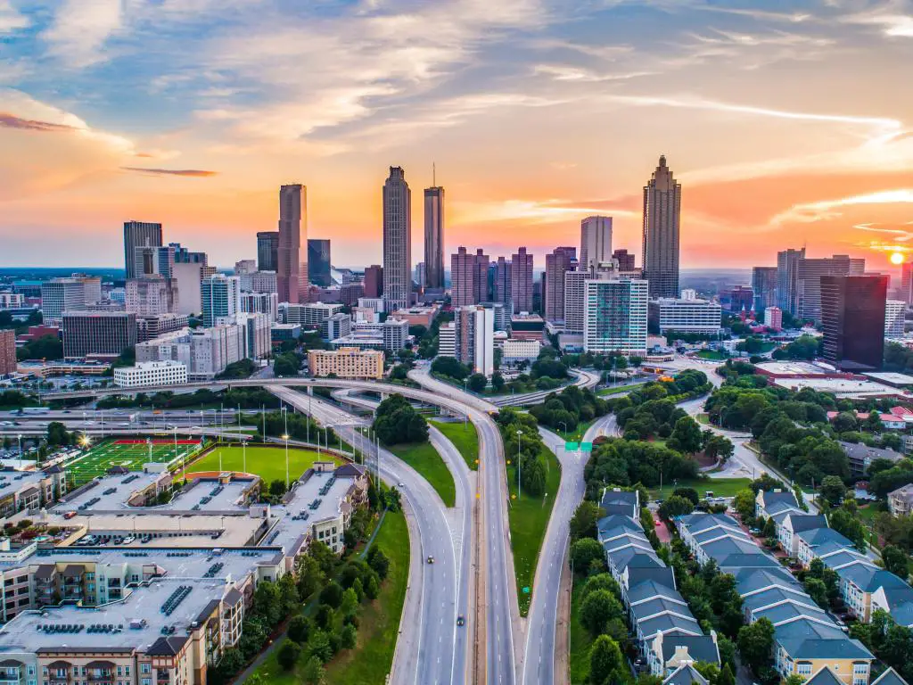 Atlanta, Georgia, EE. UU., que muestra una toma aérea del horizonte del centro de la ciudad al atardecer con los rascacielos a lo lejos y una red de caminos y césped en primer plano. 