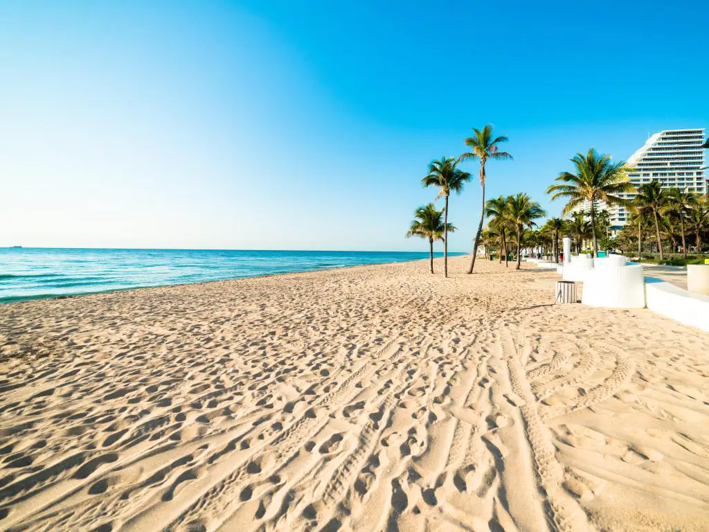 Fort Lauderdale, Florida, con una playa tranquila, arena dorada en una hermosa mañana de cielo azul con hoteles al fondo.