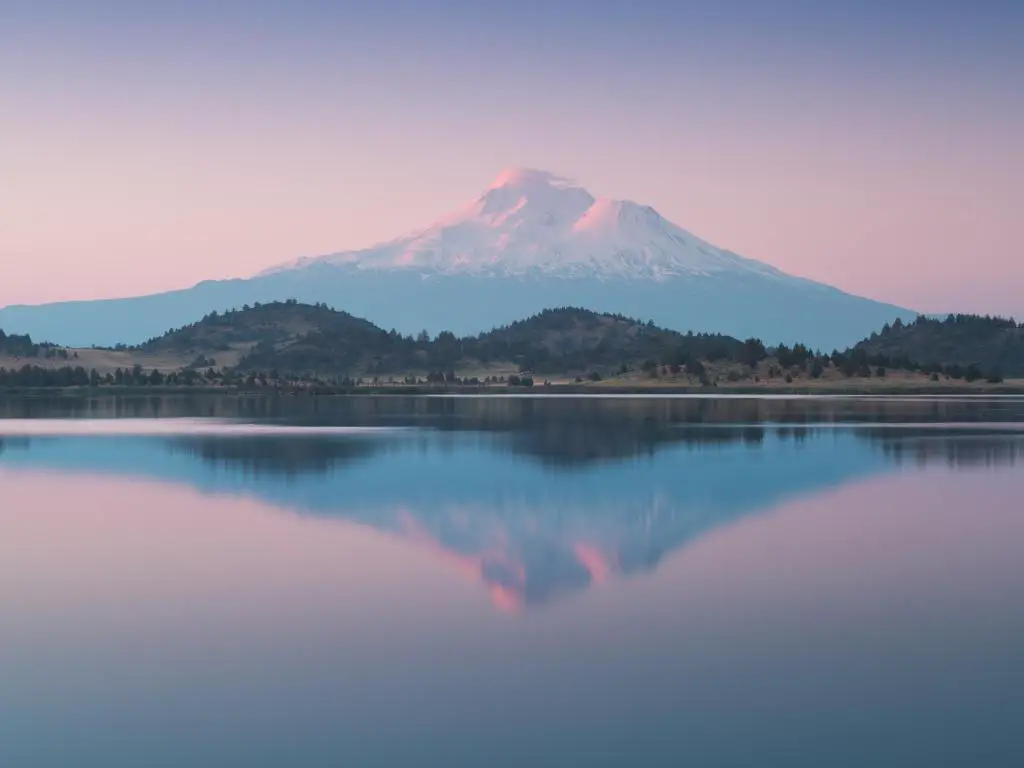 Montañas cubiertas de nieve reflejadas en un lago claro al amanecer.