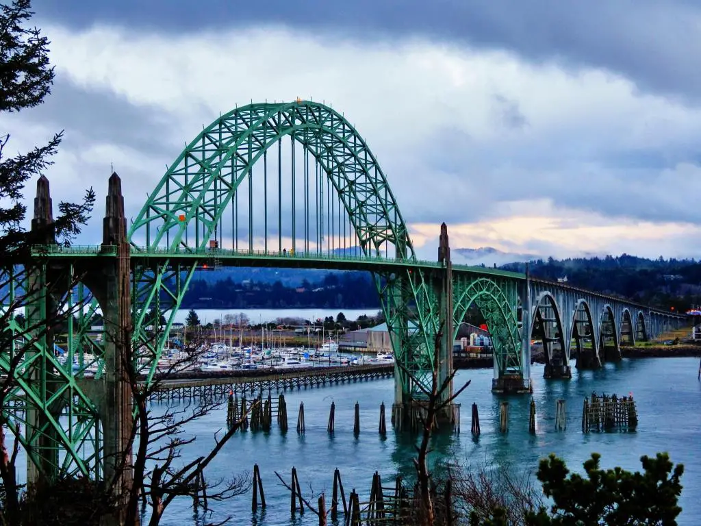 El puente de metal verde cruza un río ancho con nieve en las orillas y nubes atmosféricas