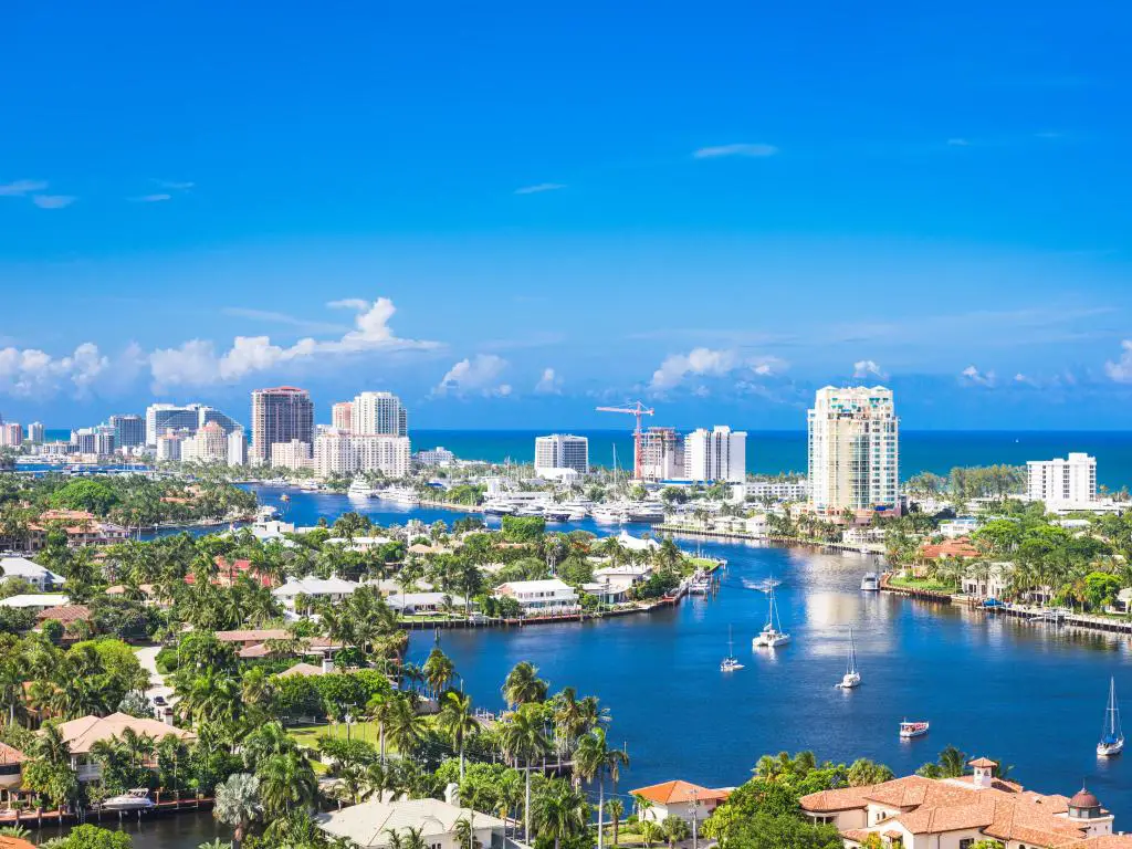 Fort Lauderdale, Florida, con yates en el agua, árboles y edificios en primer plano y los altos edificios de la ciudad en el fondo con el mar más allá. 