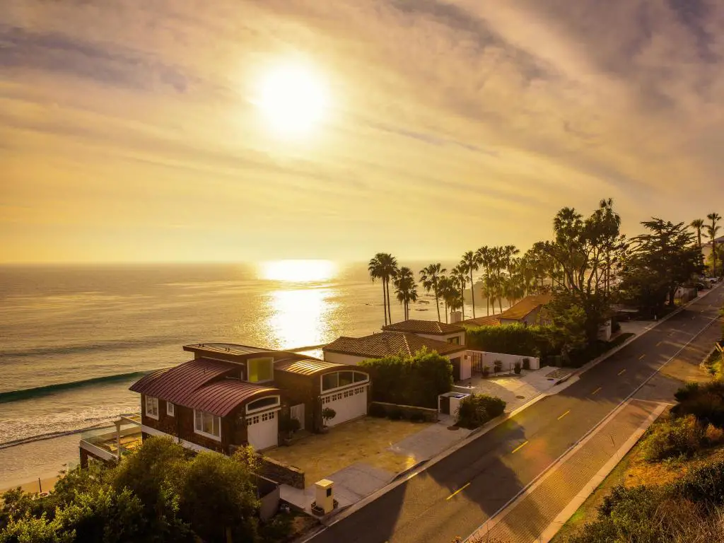 Playa de Malibu, cerca de Los Ángeles, California, con lujosas casas frente al mar con vista a la playa al atardecer, árboles en la distancia.