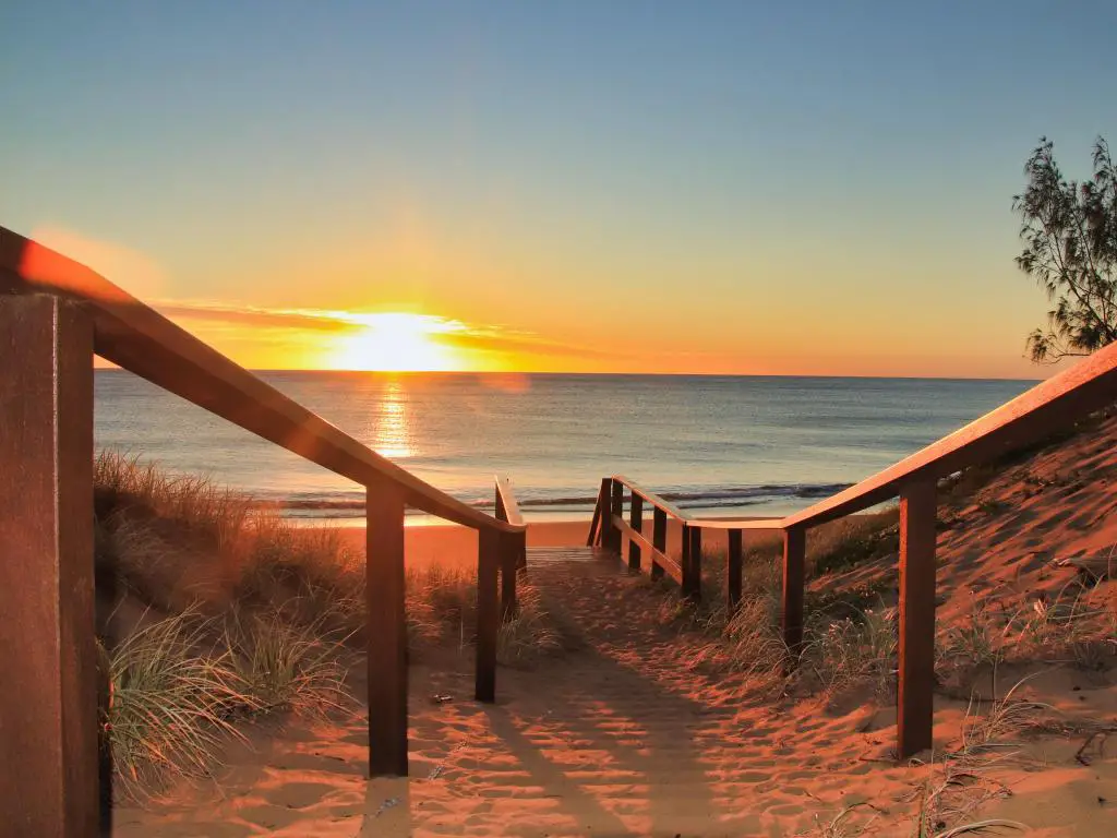 La luz dorada del amanecer ilumina la playa de arena dorada con escalones de madera a la playa sobre las dunas