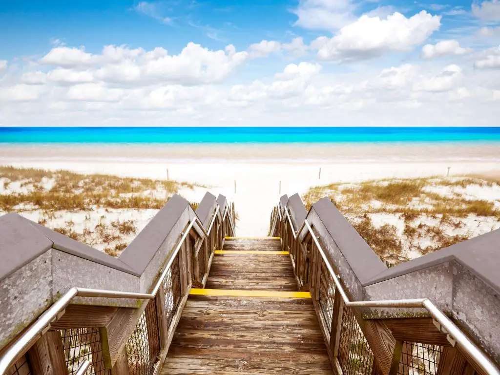 Henderson State Park, Florida, que muestra escalones de madera hasta una playa dorada con un mar azul brillante en el fondo.  
