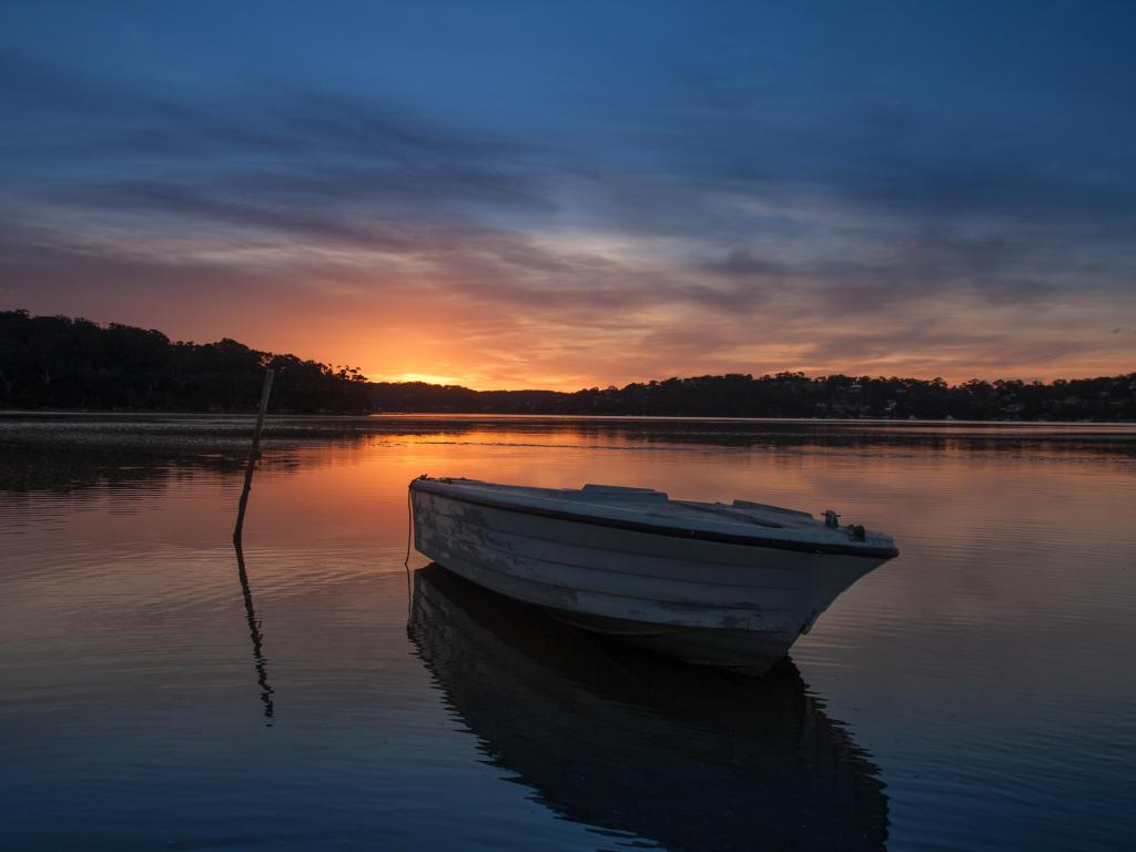 Pequeño bote amarrado en el lago al atardecer con la luz del sol rosa reflejada en el agua y los árboles que se muestran en silueta 