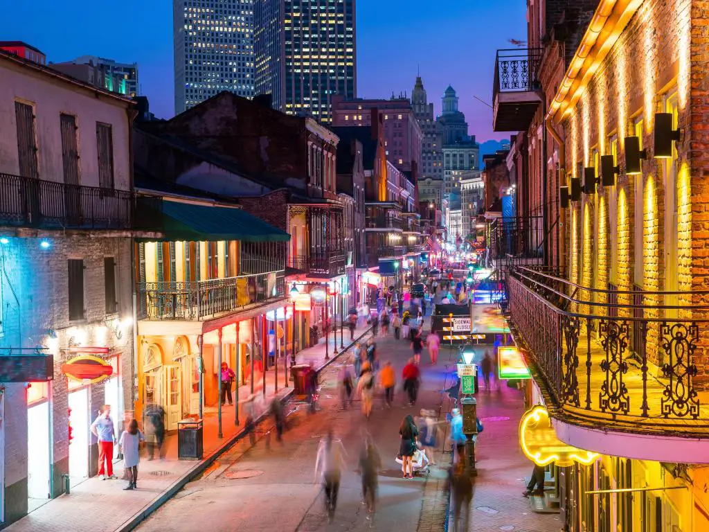 Nueva Orleans, mostrando los pubs y bares con luces de neón en el Barrio Francés de noche con gente caminando en las calles y un rascacielos al fondo. 