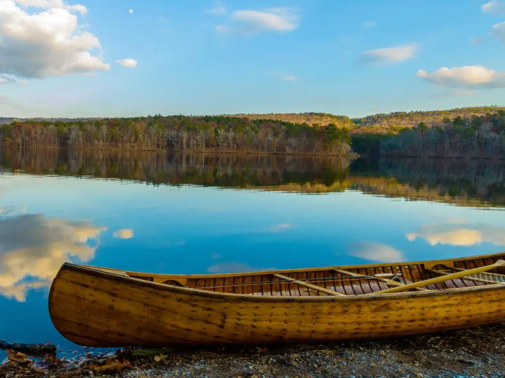 Oak Mountain State Park, Birmingham, EE. UU. en otoño con un barco de madera en primer plano en tierra, hermosas aguas que reflejan el cielo azul y los árboles en el fondo.