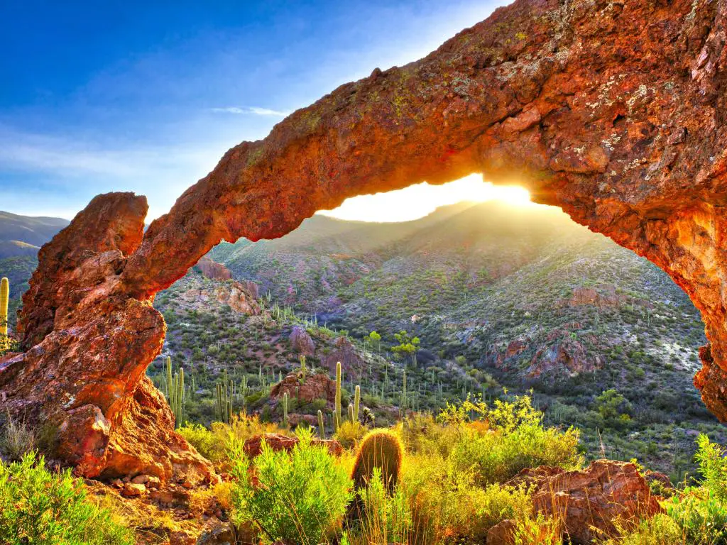 Vista del desierto a través del arco rocoso con el amanecer proyectando un brillante rayo de luz