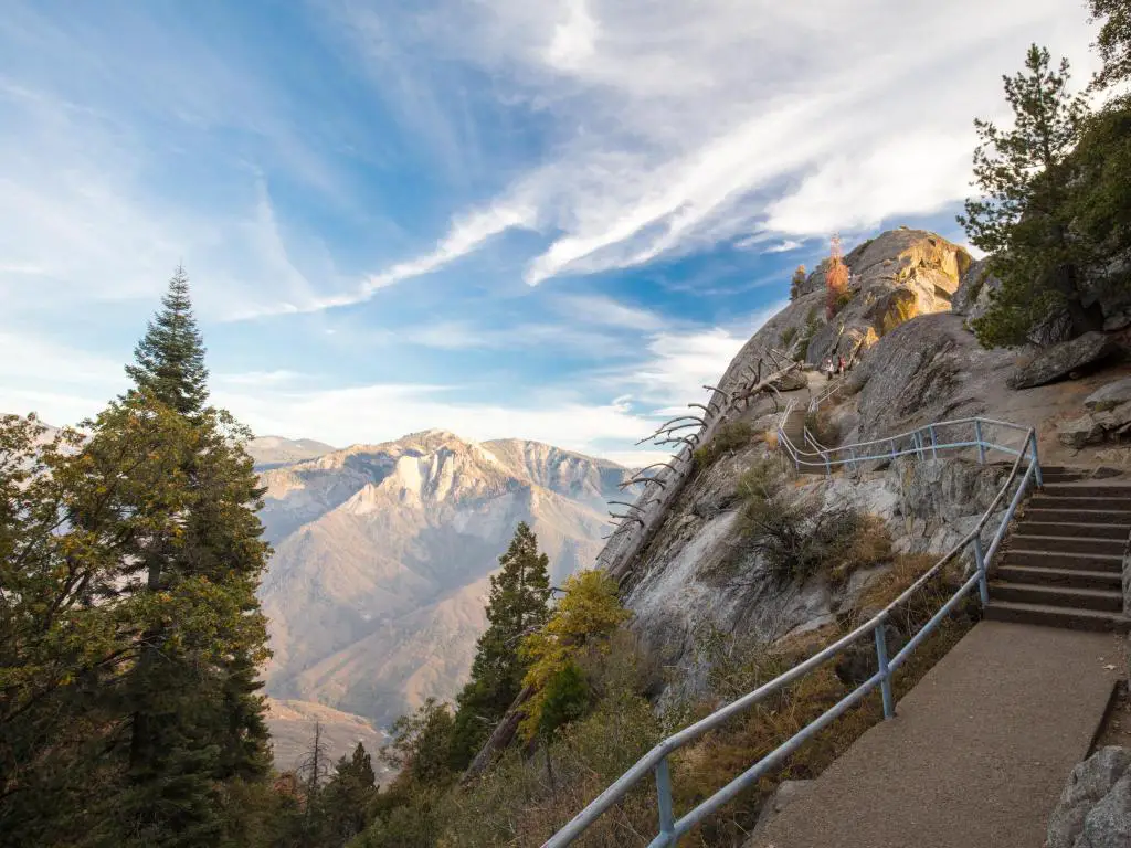 Parque Nacional Sequoia, California al atardecer en una tarde de otoño en Moro Rock con escalones junto a la montaña y árboles en primer plano, además de más montañas en la distancia. 