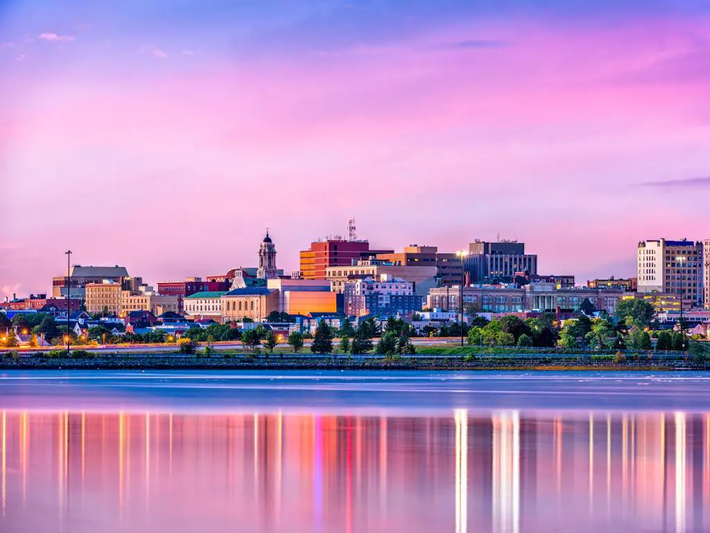 Portland, Maine al atardecer con el horizonte del centro en el fondo debajo de un cielo rosado y reflejado en el agua en primer plano.