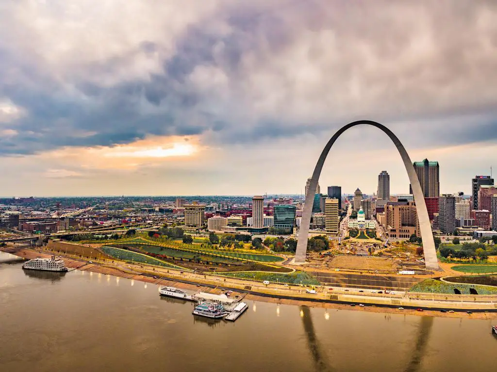 St. Louis, EE.UU. con el río en primer plano y la ciudad y el famoso arco de pie orgulloso bajo un cielo nublado.