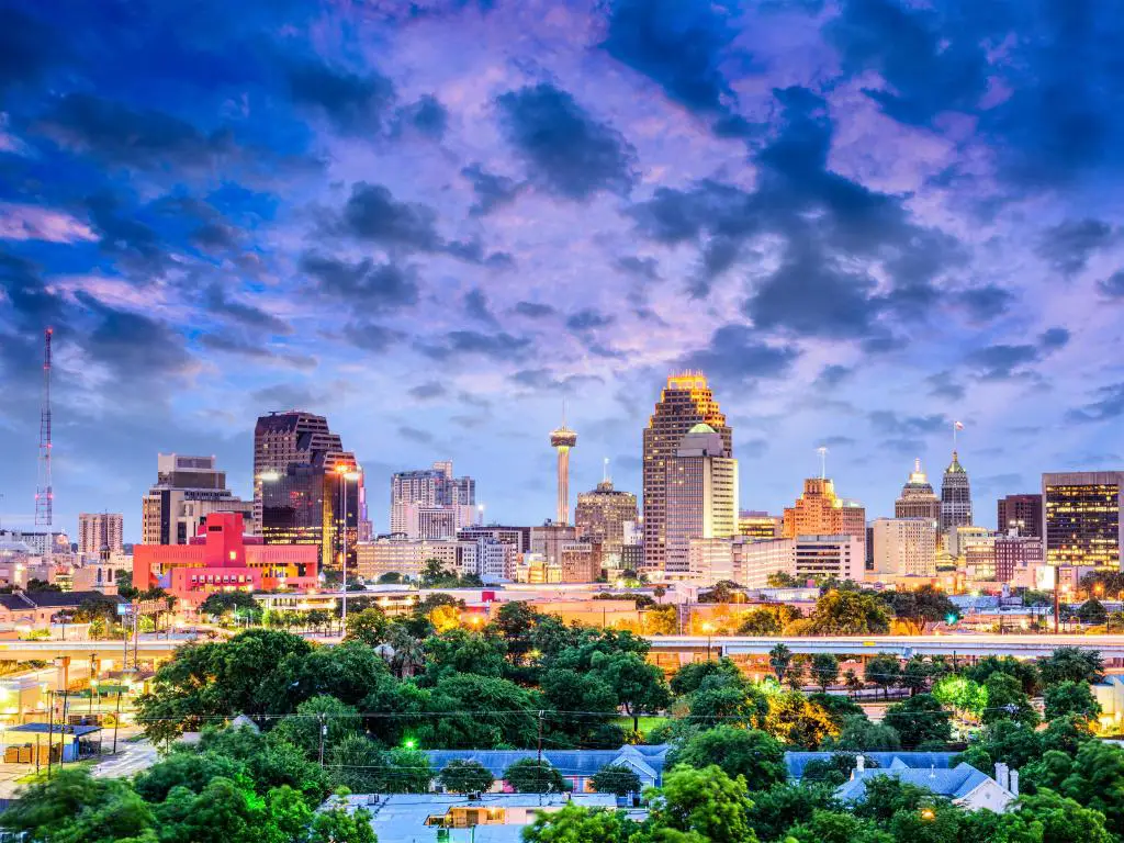 El centro de San Antonio, Texas, EE.UU. con el horizonte de la ciudad a lo lejos y árboles verdes en primer plano al atardecer con un cielo espectacular.