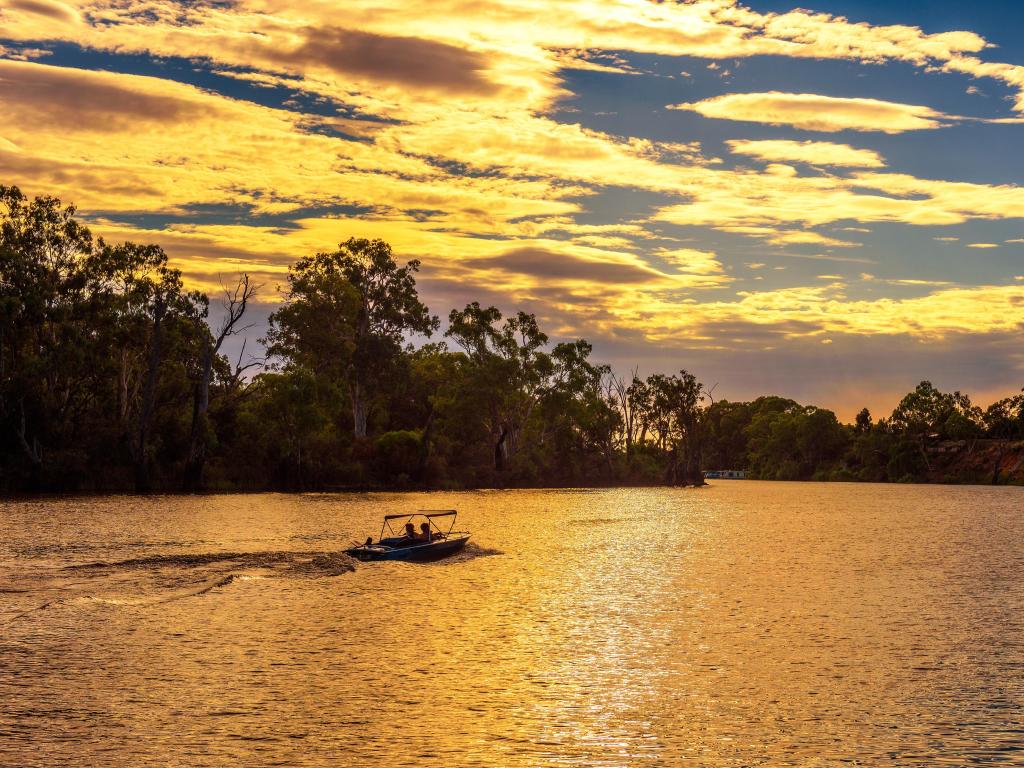 El ancho río se iluminó con la luz dorada del atardecer con siluetas de árboles en la orilla y gente montando en un bote pequeño