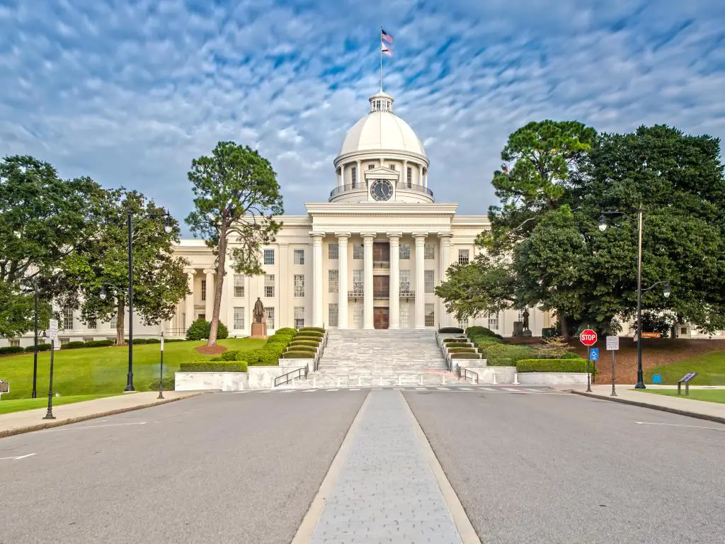 Capitolio del estado de Alabama, Montgomery con una carretera en primer plano que conduce al edificio histórico, árboles altos a ambos lados de la carretera en un día nublado.