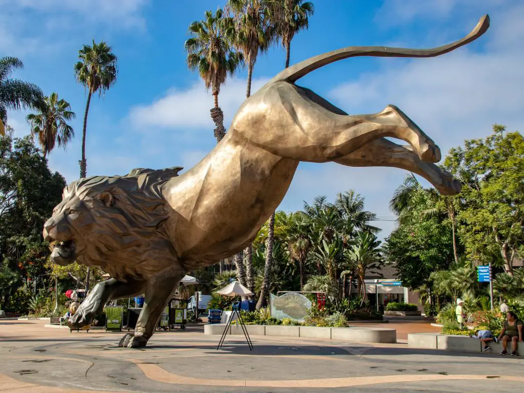 Estatua de león a la entrada del zoológico de San Diego con palmeras en el fondo y un cielo azul.