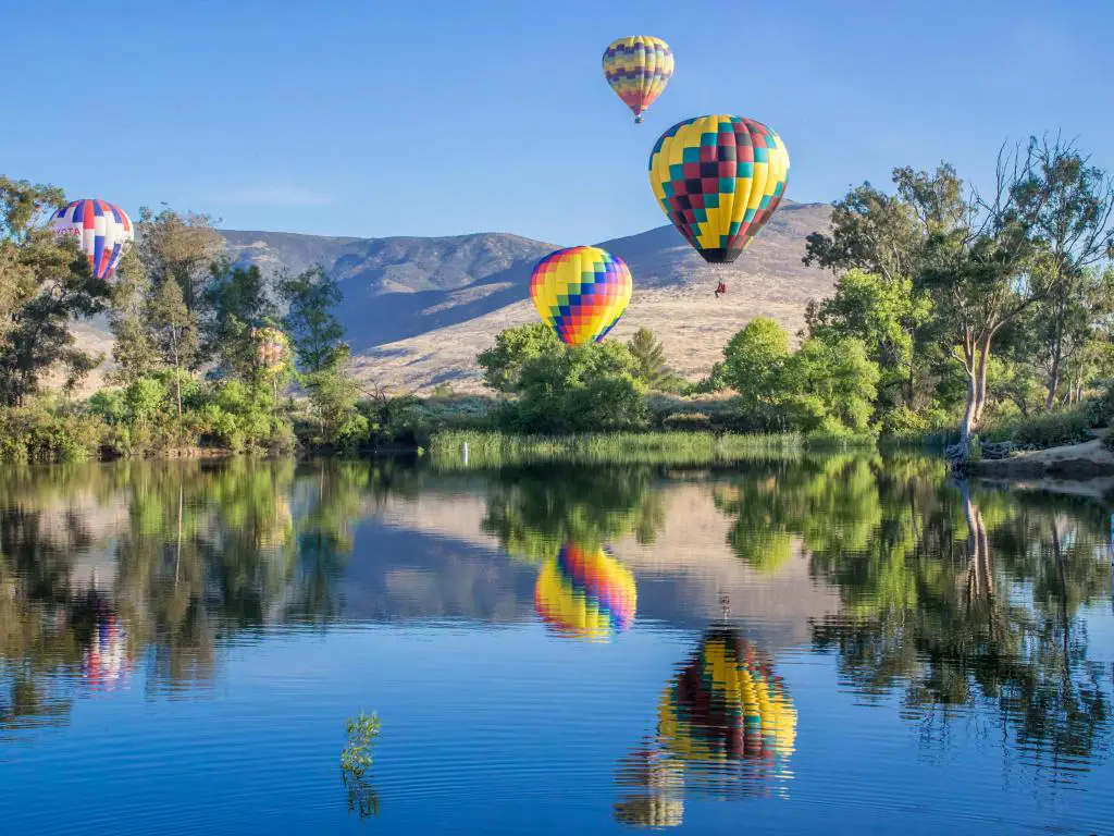 Montañas en el fondo, con coloridos globos aerostáticos en el aire que se reflejan en el lago.