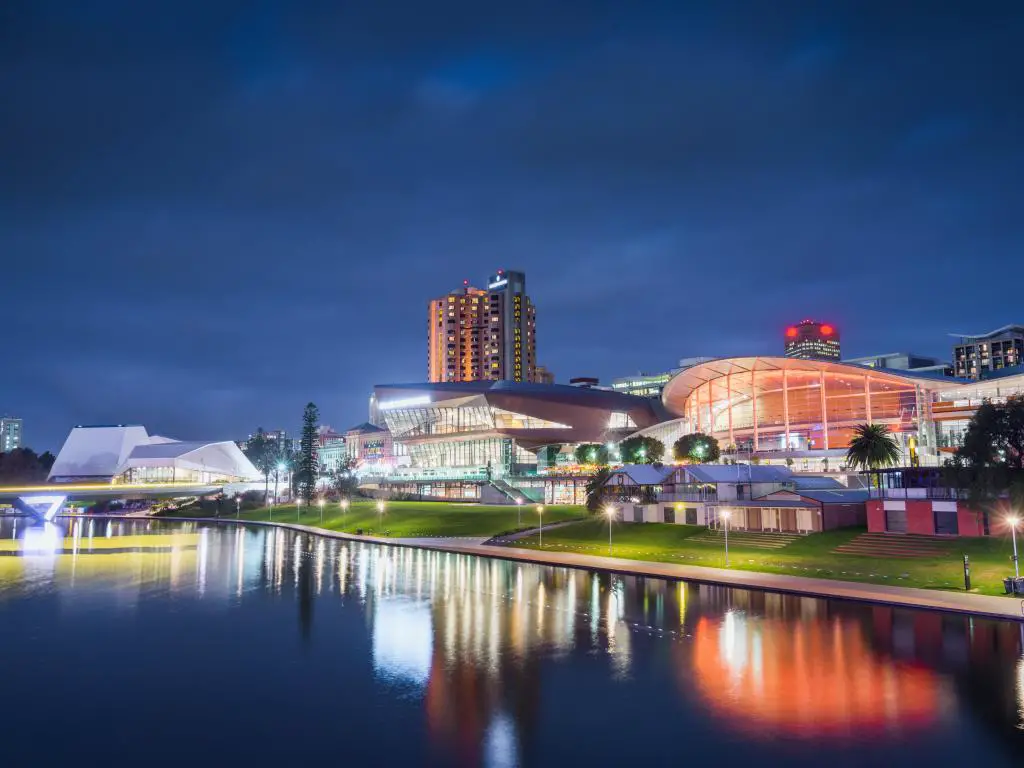 Adelaide, Australia por la noche con agua en primer plano que refleja los edificios que están iluminados con luces y farolas.