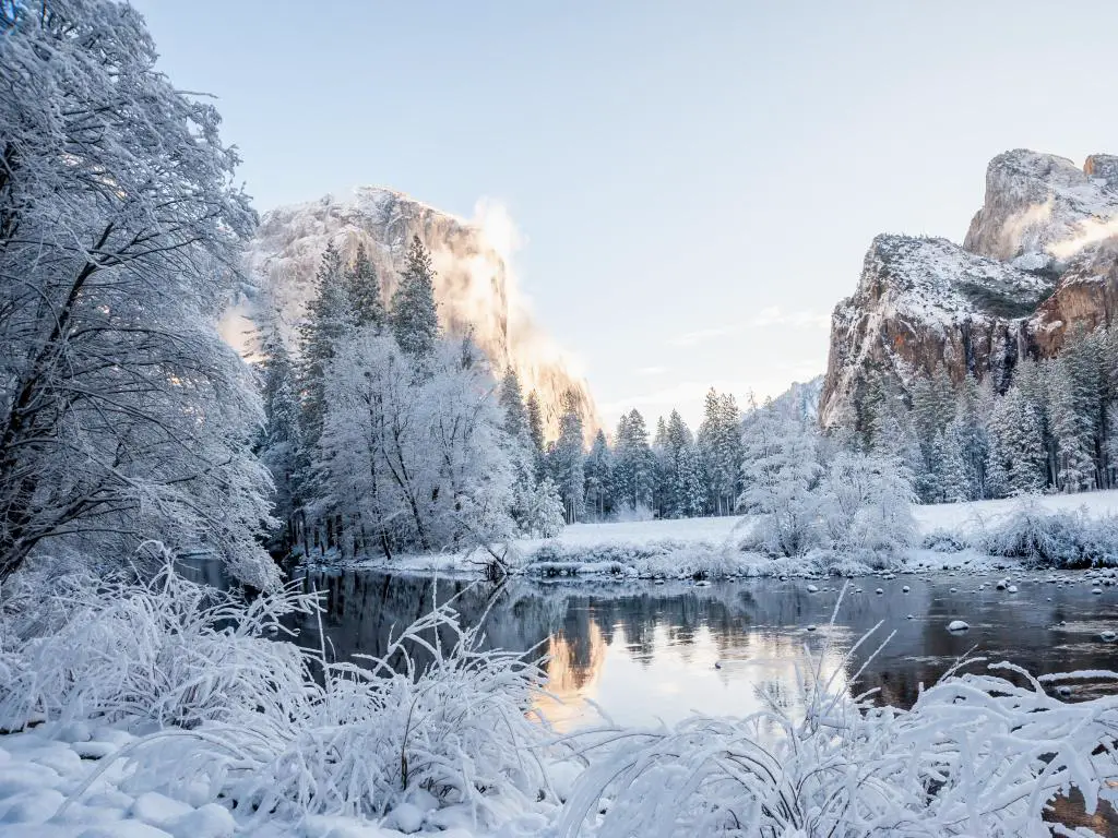 Agua clara que refleja árboles cubiertos de nieve con acantilados rocosos