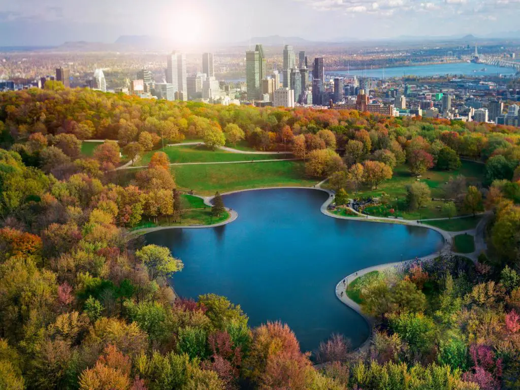 Montreal, Canadá en otoño con árboles que bordean un gran lago en el medio y la ciudad de Montreal en el fondo. 