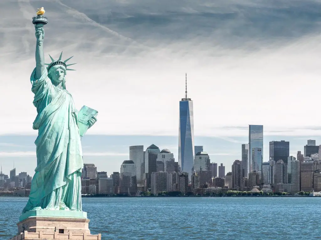 Horizonte de la ciudad de Nueva York con la Estatua de la Libertad en primer plano con el río Hudson y un cielo gris arriba
