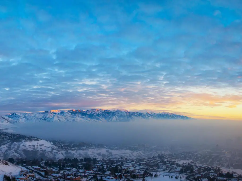 Salt Lake City al atardecer con smog cubriendo el lago y montañas nevadas en primer plano y fondo. 