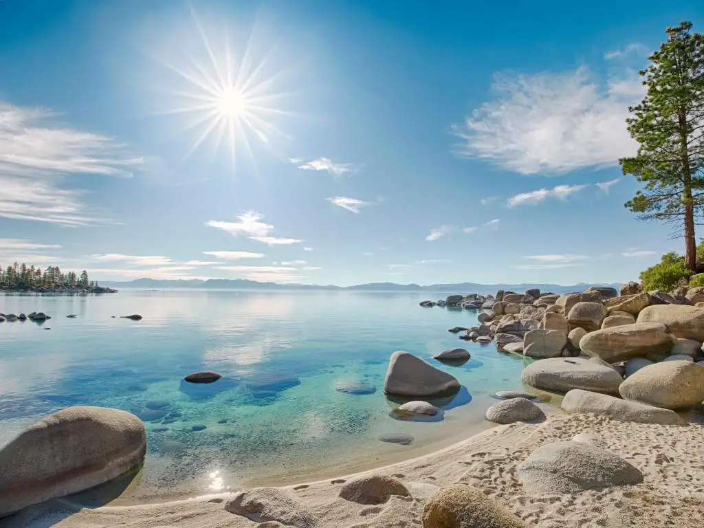 El lago Tahoe con una playa de arena y grandes rocas a la izquierda y un tranquilo mar turquesa en un día soleado.