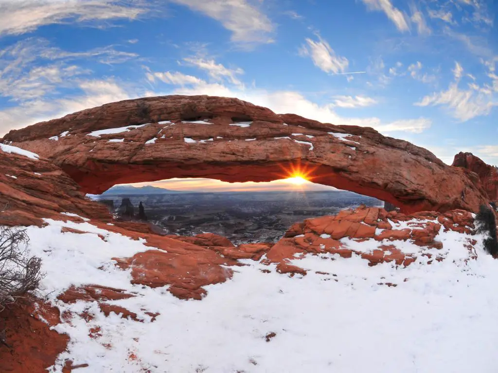 Sol brillando a través de un arco natural en el Parque Nacional Canyonlands, Utah, en invierno, con nieve por todas partes