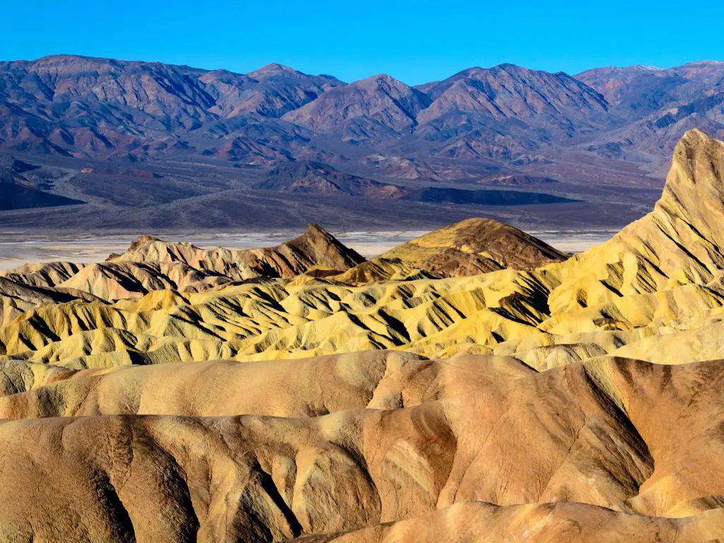 Parque Nacional del Valle de la Muerte con formaciones rocosas doradas en primer plano y montañas más oscuras en el fondo. 