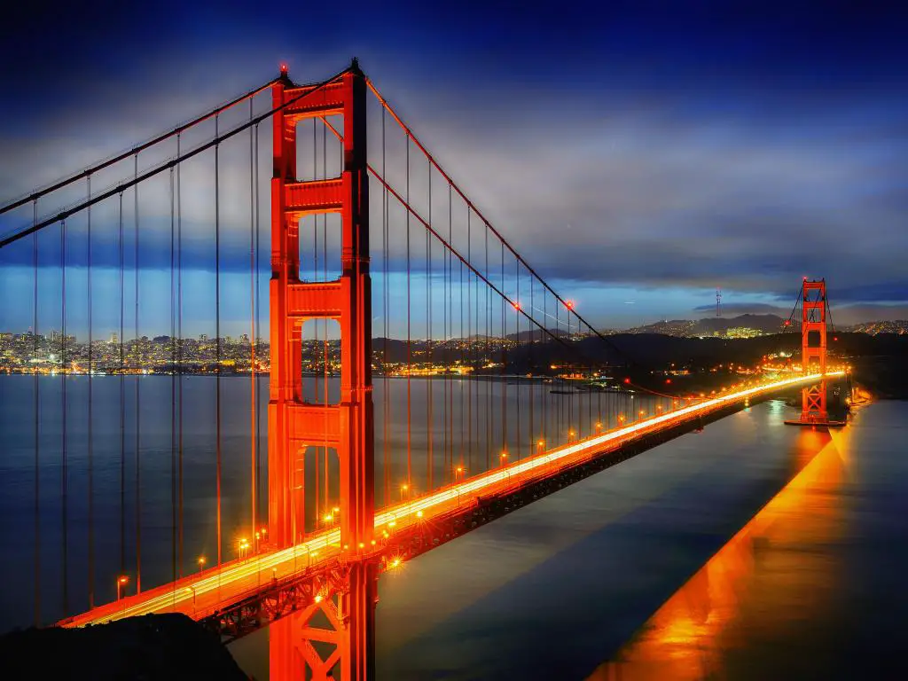 Puente Golden Gate, San Francisco de noche, con San Francisco a lo lejos y el puente iluminado en amarillos, rojos y naranjas.
