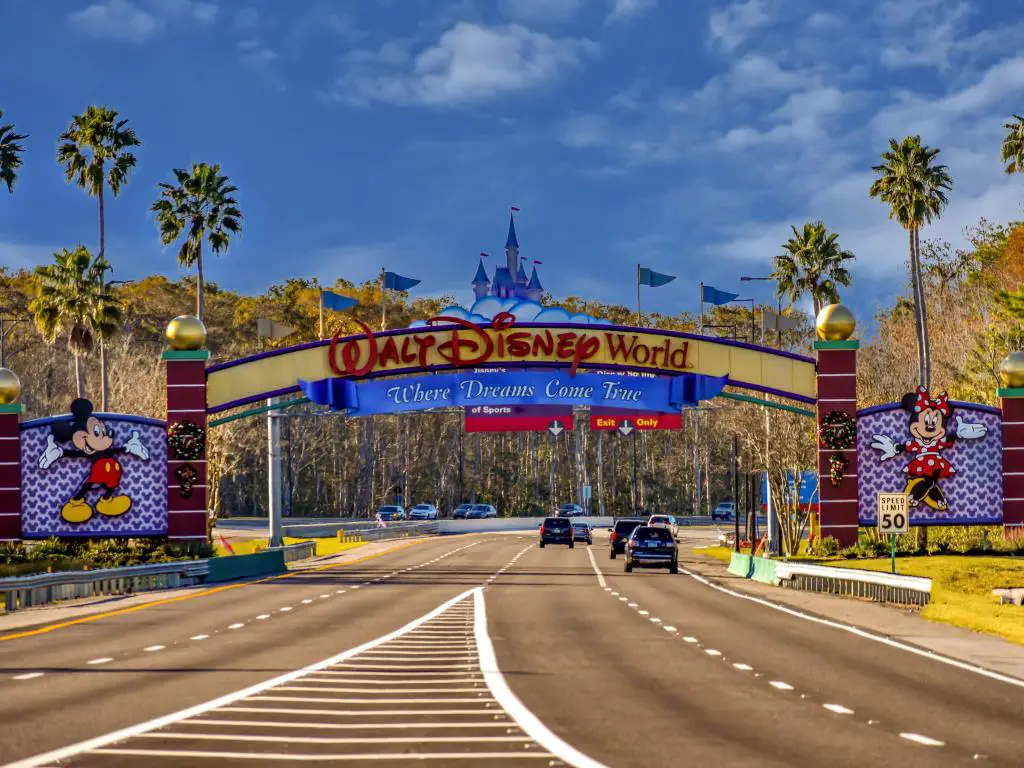 Coches circulando por una carretera bajo el arco de entrada de Walt Disney World en Orlando, Florida, con un cielo azul arriba.