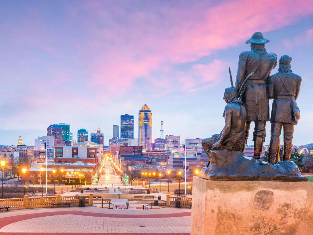 Pioneros de la estatua del Territorio con vistas al horizonte de la ciudad de Des Moines, Iowa al atardecer.