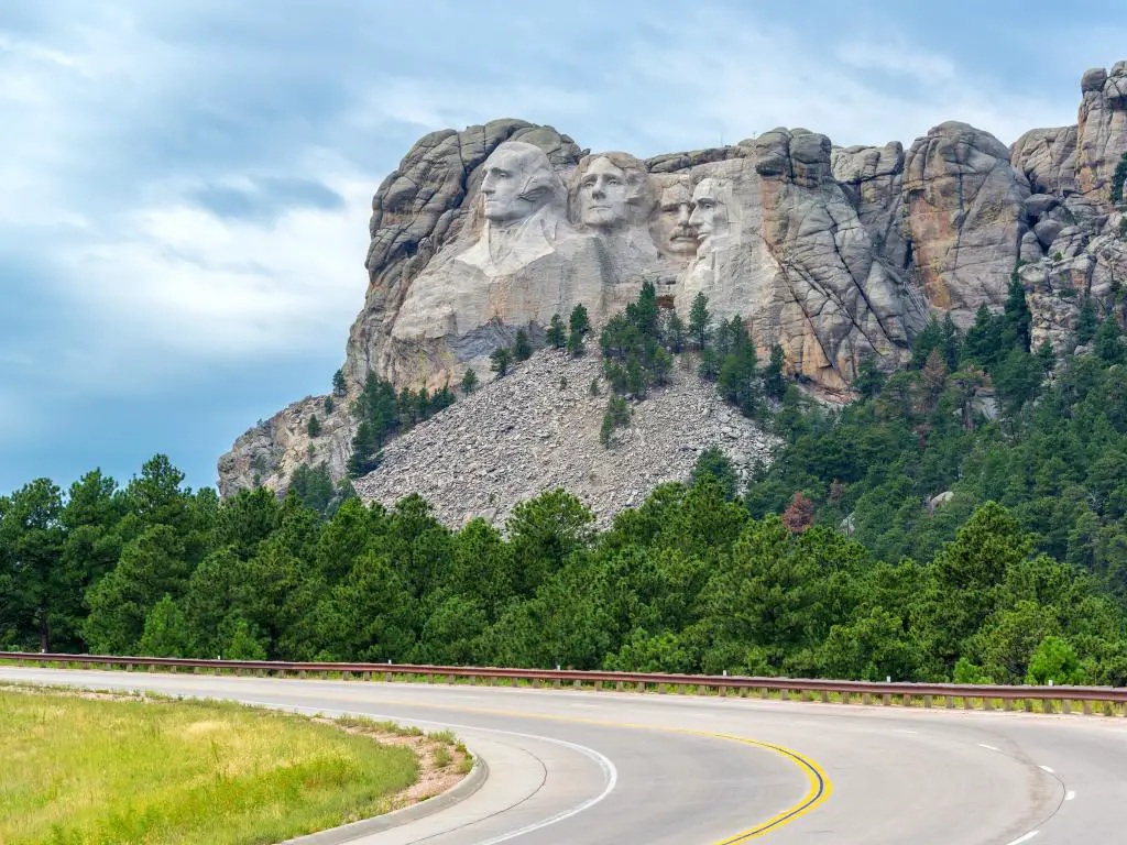 Una carretera curva vacía que conduce al Monumento Nacional Monte Rushmore en Dakota del Sur y una vista de los rostros tallados de los Cuatro Presidentes de los Estados Unidos en la montaña y los árboles verdes