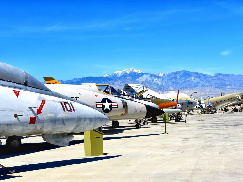 Una línea de aviones antiguos de la Segunda Guerra Mundial que se pueden volar se exhibe afuera en un día soleado con una vista de las montañas desde lejos en el Museo del Aire de Palm Springs.