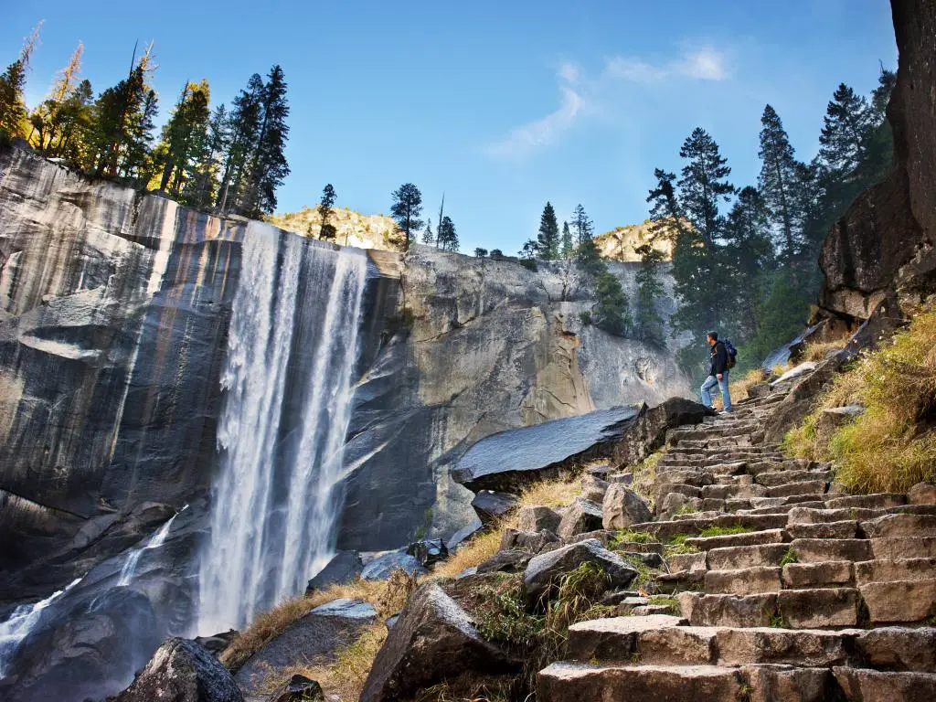Un hombre en lo alto de las escaleras de roca disfruta de la belleza escénica de las cascadas en el Parque Nacional Yosemite. 