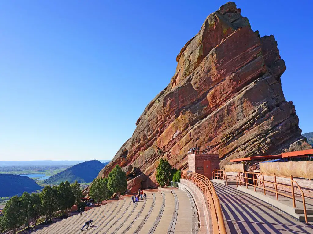 Una vista pintoresca del histórico anfiteatro Red Rocks al aire libre con un par de personas sentadas en los bancos disfrutando de la vista de las montañas desde lejos temprano en la mañana en Denver