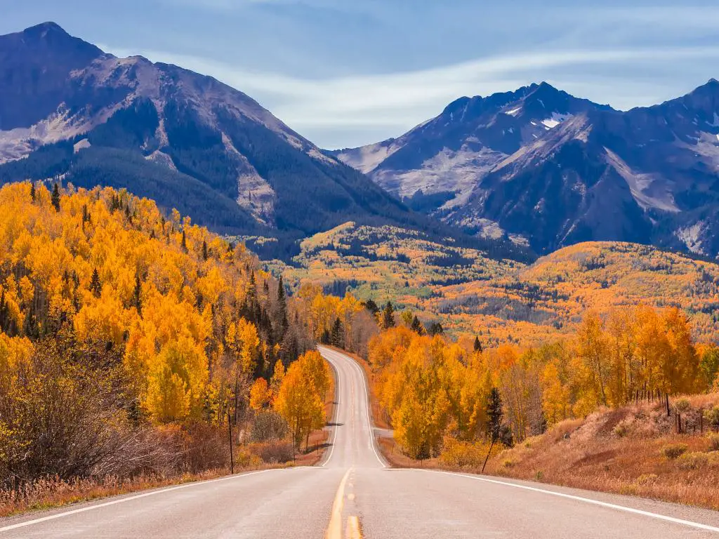 Una carretera vacía de la autopista 45 cerca de Telluride, Colorado, con árboles durante el otoño y una vista de las montañas por delante.
