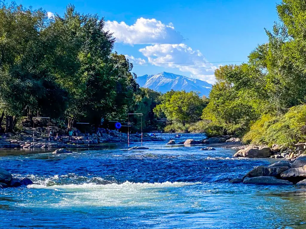 Una imagen del río Arkansas que fluye cerca de Salida, Colorado, con árboles y un pico de montaña durante un día soleado.