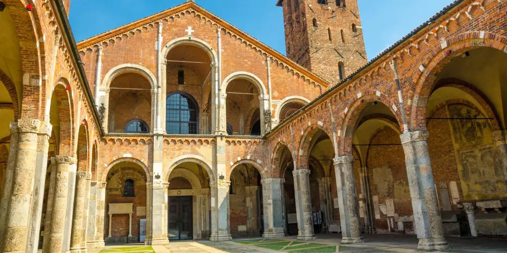 Basílica de la iglesia de Sant'Ambrogio en Milán, Italia, con campanarios, patio, arcos y fondo de cielo azul