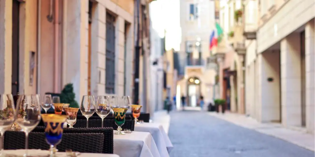 Copas de vino sentados en mesas fuera de un restaurante en una calle adoquinada en Bolonia, Italia