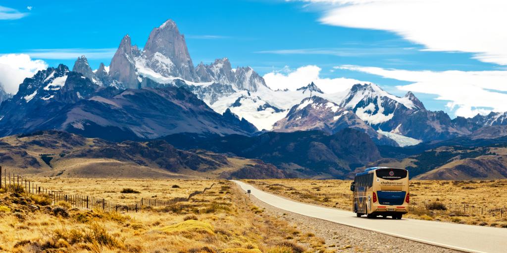 Un autobús circulando por una carretera desierta hacia unas montañas cubiertas de nieve en Argentina 