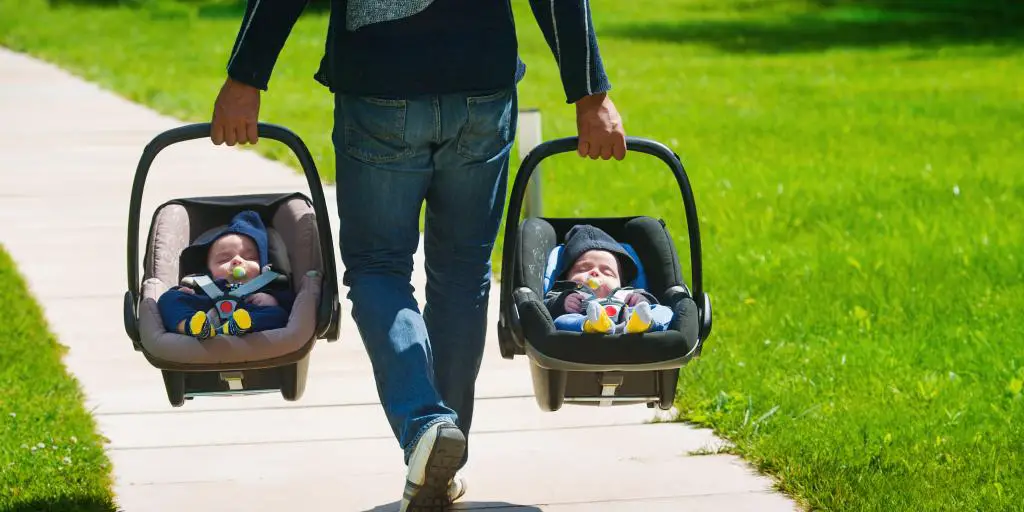Padre caminando junto con dos bebés en asientos de auto