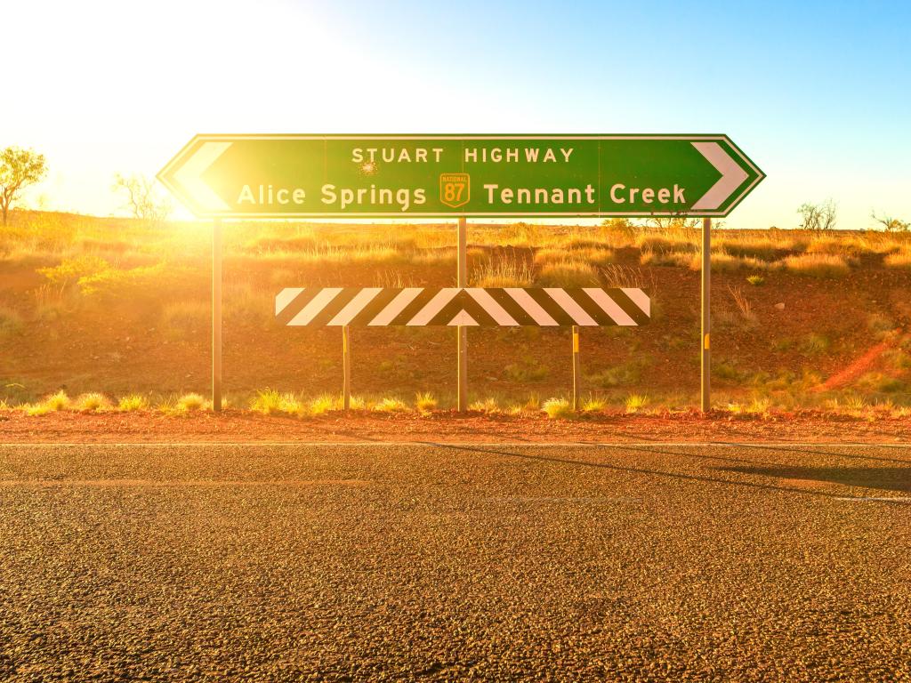 Firmar en la Stuart Highway en el Territorio del Norte de Australia mostrando el camino a Alice Spings y Tennant Creek con el sol detrás