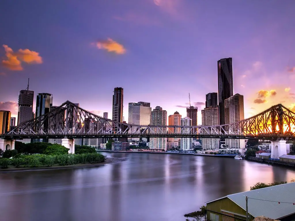 Puente sobre el río gris acero con edificios altos en la orilla, cielo azul púrpura y luz brillante del sol poniente
