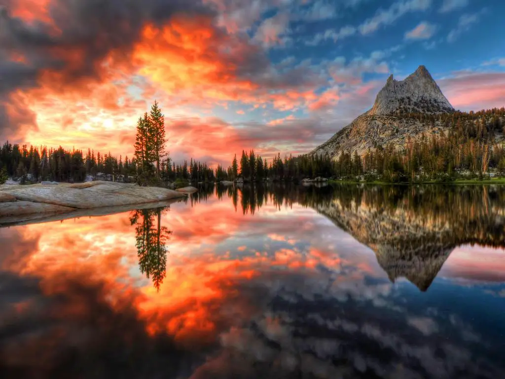 Parque Nacional Yosemite, California al atardecer con un espectacular cielo rojo sobre el lago Cathedral y una montaña distante que se refleja en él.
