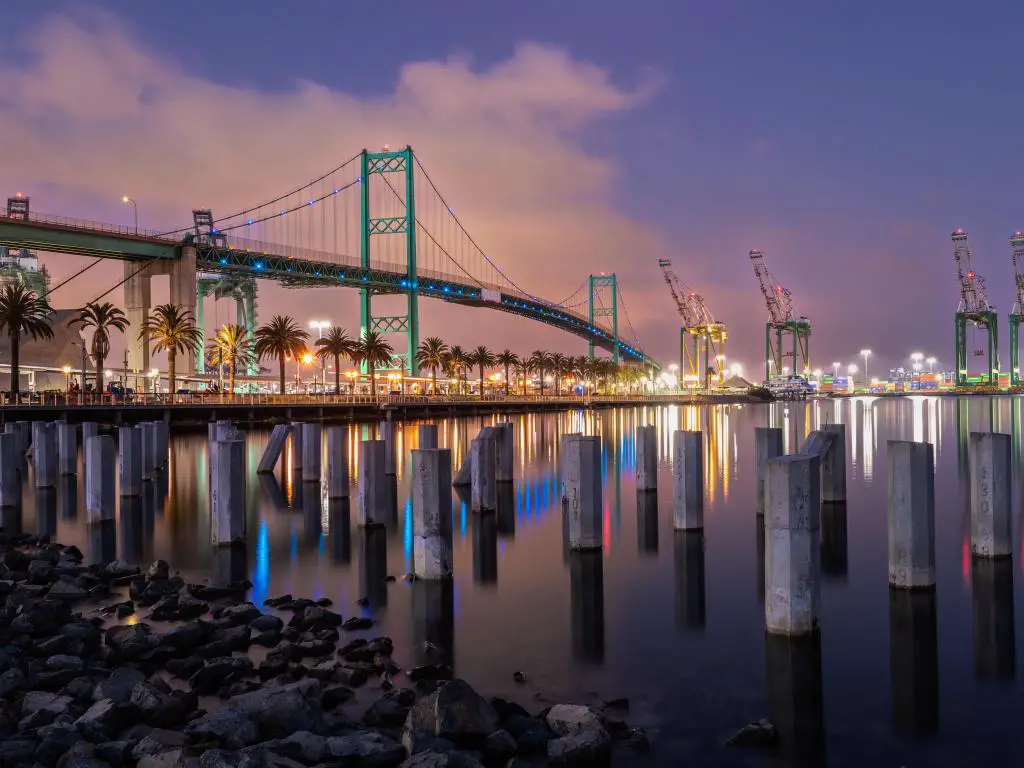 Long Beach, CA, EE.UU. con el puente Vincent Thomas que conecta Long Beach y San Pedro tomado de noche con árboles que bordean el borde del agua. 