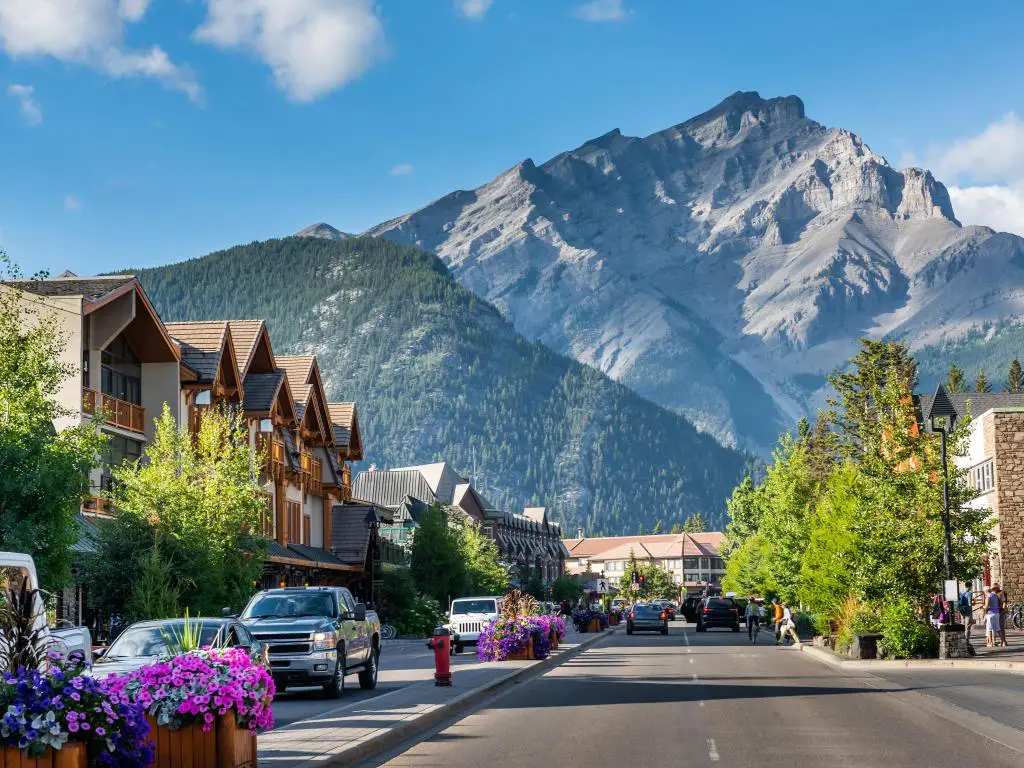 Banff, Alberta, Canadá, con una calle y una hilera de casas en primer plano y las impresionantes montañas a lo lejos en un día soleado.