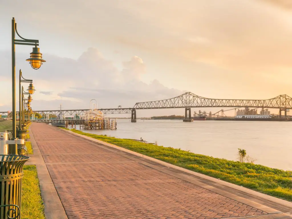 Baton Rouge, Luisiana, con un camino a lo largo del río Mississippi, farolas a un lado y un resplandor vespertino y el puente al fondo.