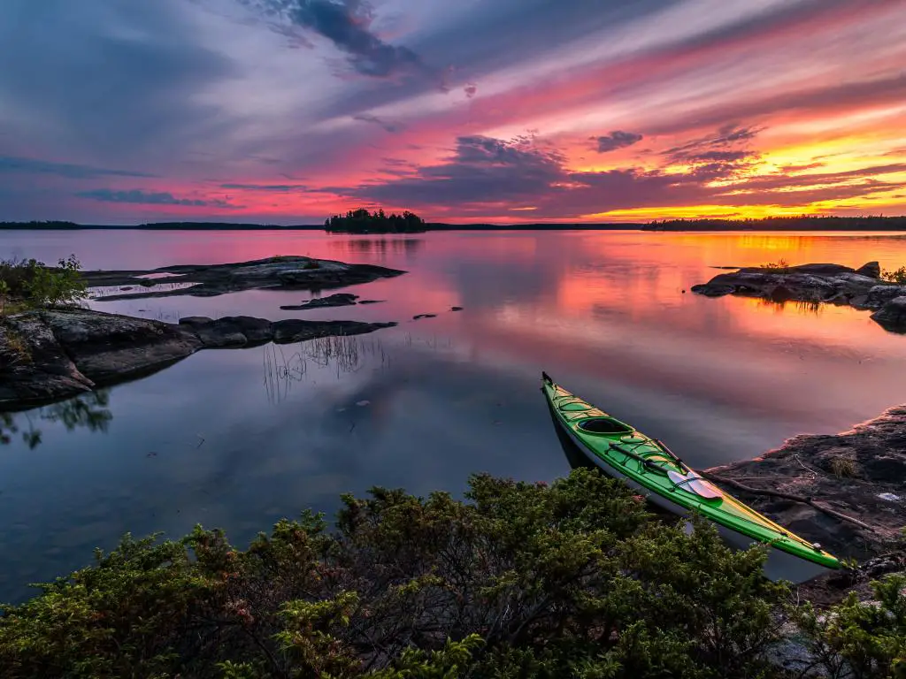 Eagle Lake, noroeste de Ontario, Canadá, con un kayak detenido en la orilla del lago Eagle al atardecer en primer plano y el agua tranquila que conduce a la distancia. 