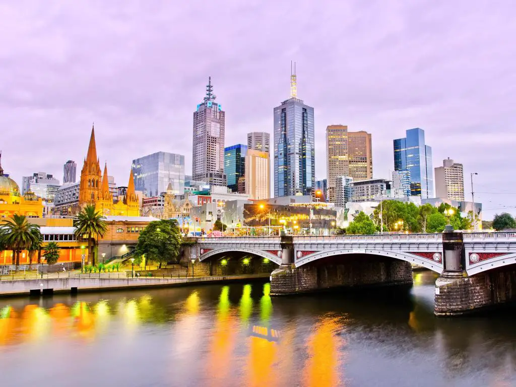 Edificios de gran altura del horizonte de Melbourne al atardecer a través del río con puente